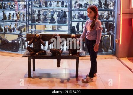 Sharm El Sheikh, Egypt - November 20, 2021: Little girl is standing near the sculptural composition depicting three funny monkeys sitting on bench Stock Photo