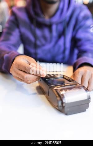 Crop unrecognizable African American male client using bank card for contactless payment with NFC technology via wireless terminal in cafe Stock Photo