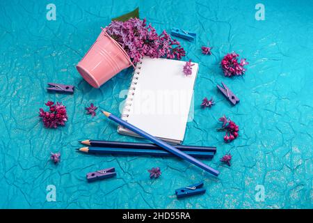 Blank notebook, pencils and lilac flowers on vintage painted blue cardboard background Stock Photo