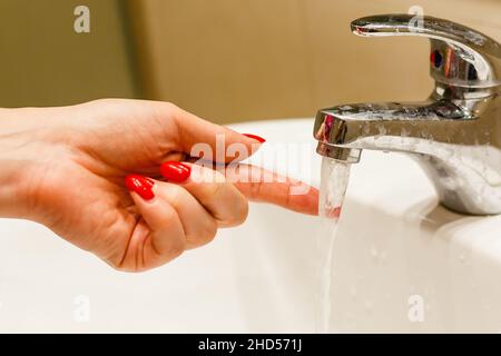 Closeup on fingers near faucet of sink or bathtub in home bathroom. Female at home checking running water touching with hand Stock Photo