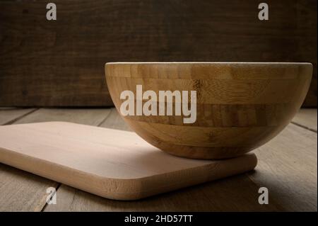 Empty bowl and wooden chopping board on a dark, rustic wooden background  Stock Photo