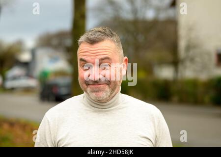 Charismatic man grinning at the camera in amusement with a knowing expression outdoors on an urban street in autumn Stock Photo