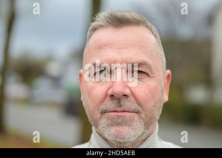 Headshot of a bearded senior man looking at the camera with a serious thoughtful expression outdoors in an urban street Stock Photo