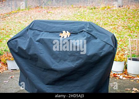 An autumn leaf has fallen on a covered barbecue grill signifying the end of the barbecue season Stock Photo