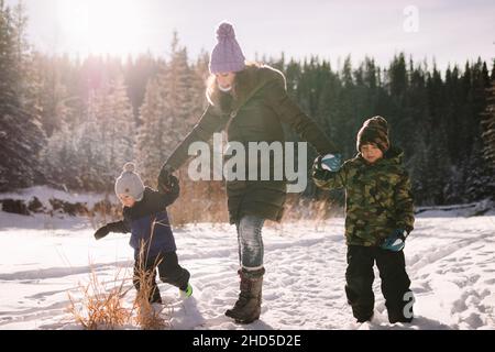 Woman and two children holding hands and walking along a snowy footpath on a sunny day Stock Photo