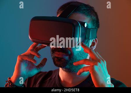 Young man in VR glasses close up portrait virtual reality in color neon light, future technology, education video gaming Stock Photo