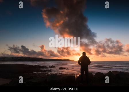 The figure of a man silhouetted by an intense sunset over Fistral Bay in Newquay on the North Cornwall coast. Stock Photo