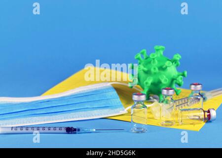 Corina virus booster vaccination concept with 4 vials and syringes, vaccination passport, virus model and face mask on blue background Stock Photo