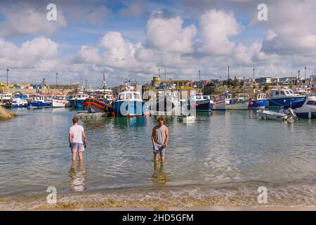 Two men standing in the sea in the historic picturesque working Newquay Harbour in Newquay in Cornwall. Stock Photo