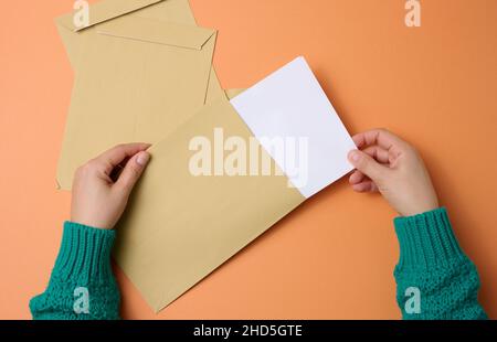 female hand holds paper envelopes on an orange background, top view. Correspondence Stock Photo