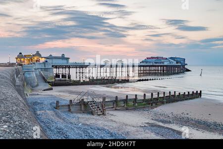 Dusk over Cromer pier captured next to two wooden groynes. Stock Photo