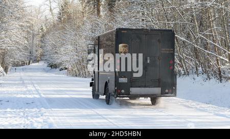 Carnation, WA, USA - December 29, 2021; A UPS delivery truck drives on a snow covered road with  winter trees Stock Photo