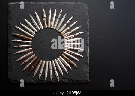 Steel dip pen nibs arranged in a circle, isolated on black stone tile texture Stock Photo