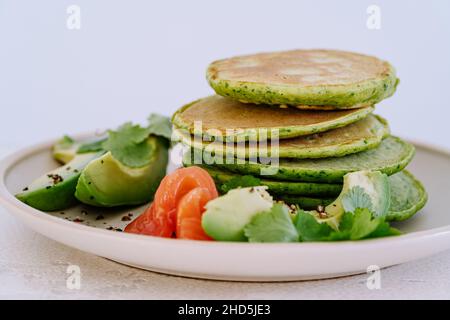 Spinach pancakes with avocado and salted salmon on light background close up, healthy breakfast or brunch Stock Photo