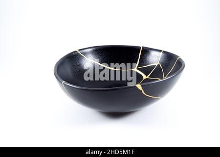 kintsugi gold cracks restoration, Japanese black bowl fixed with the antique kintsukuroi restoration technique, the beauty of imperfections, represent Stock Photo