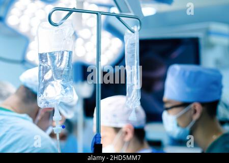 Selective focus on saline transparent plastic bag. Medical dropper in the operating room. Surgery on a blurred background. Stock Photo