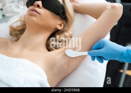 Applying a transparent gel before the laser hair removal procedure to the armpit area. Underarm epilation process Stock Photo