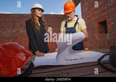 Woman engineer looking to side while worker studying blueprints Stock Photo