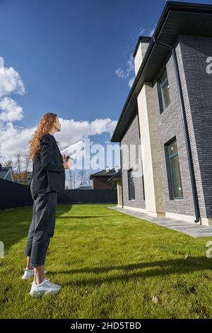 Female engineer is inspecting house from lawn Stock Photo