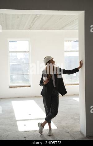 Woman looking at wall while standing with blueprints in room Stock Photo