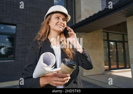 Female having phone conversation outdoors holding drawings and coffee Stock Photo