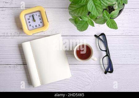 Flat lay of notepad, coffee, clock, eyeglasses and green plant on white wood table. Copy space. Stock Photo