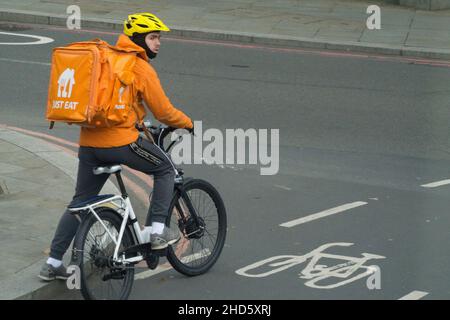 London, UK, 3 January 2022: A Just Eat delivery rider on a bicycle waits in the cycle lane at a junction. Along with Uber Eats and Deliveroo, delivering hot food to customers is a growth sector. Anna Watson/Alamy Live News Stock Photo