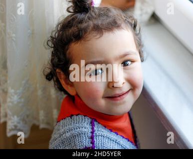 Close up portrait of beautiful little child girl looking at the camera and smiling happily at home. Happy childhood concept idea