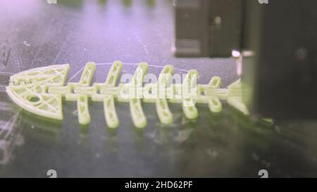 Close Up of 3D printer while printing fish form. Plastic skeleton of fish lies on a white background. It is printed on a 3d printer. A very beautifull Stock Photo