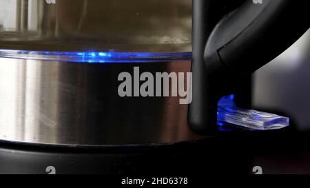 Male finger pressing the power switch on the electric kettle. Close up of process of heating clean drinking water in a kettle with blue led illuminati Stock Photo