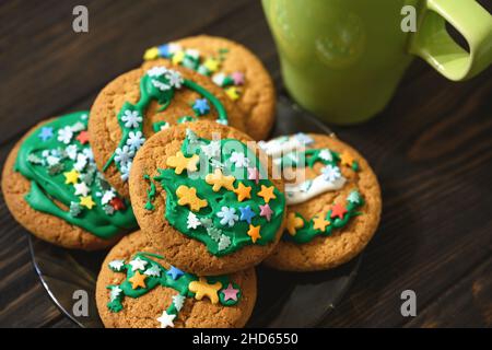 Oatmeal cookies on plate and coffee cup on wooden table, homemade Christmas biscuit decorated sugar glaze. Pile of dessert food close-up, delicious ea Stock Photo