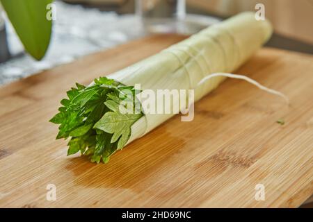 Ready-made bouquet of greens lies on a wooden board in the kitchen, for dressing dish Stock Photo