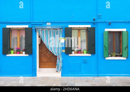 Close up of a brightly colored light-blue plaster facade with windows with flower pots and a door Stock Photo