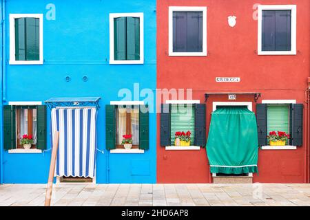 Close up of a brightly colored two-story plaster facade with windows with flower pots and two doors, the leftmost blue and the rightmost is red Stock Photo