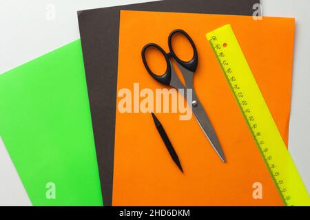 Top view of green, black and orange paper for diy and scissors, pencil and ruler on white background Stock Photo