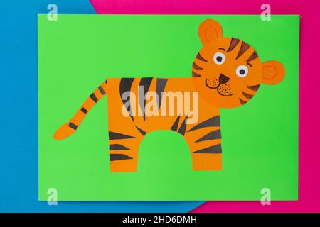 Top view of handmade orange tiger applique on green paper on blue and pink background Stock Photo