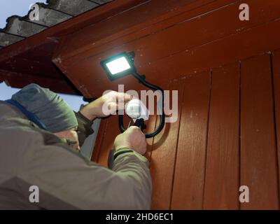 a man maintaining a motion detector and spot of light on a wall, outdoor shot Stock Photo