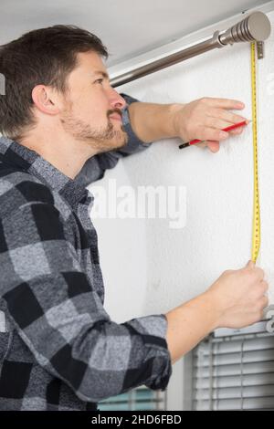 man measuring under a curtain rail Stock Photo