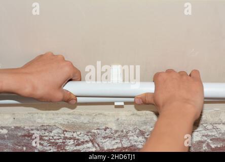 Polypropylene heating pipes installation above the floor as a part of a hydronic radiator heating system. A plumber is installing PP white pipes to co Stock Photo