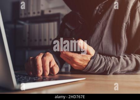 Hacker stealing data from jailbroken phone and attacking connected networks and systems, hooded male person hacking modern smart device, selective foc Stock Photo