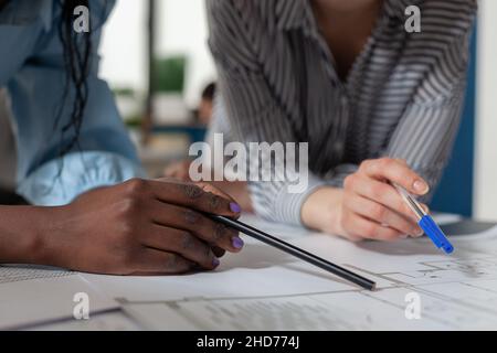Closeup of architectural engineer hands holding pencil and pen over blueprints at modern technical drawing desk. Detailed view of architects inspecting construction plans of residential project. Stock Photo