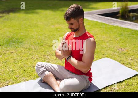 Young man sitting with hands clasped and cross-legged while meditating in park Stock Photo