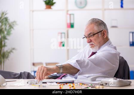 Old male drug addicted employee sitting at workplace Stock Photo