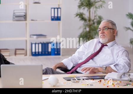 Old male drug addicted employee sitting at workplace Stock Photo