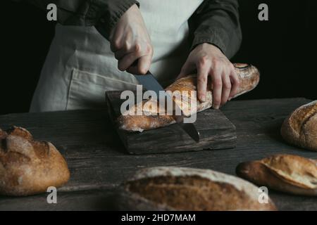 Female hands are cutting rye loaf. Bread without yeast. Concept of healthy food and traditional baking. Stock Photo