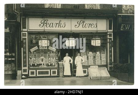 Original Edwardian postcard of Pearks Stores, grocery shop, shopfront, 2 shopkeepers stand outside. Edwardian shop / Victorian shop. The store is selling Peark's butter, famous Huntley and Palmers biscuits, fresh eggs  Xmas fruit, homemade mincemeat at Christmas time, circa 1910, U.K. Stock Photo