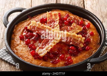 Aggakaga is a traditional South Swedish thick pancake with fried bacon and lingonberries closeup in the pan on the wooden table. Horizontal Stock Photo