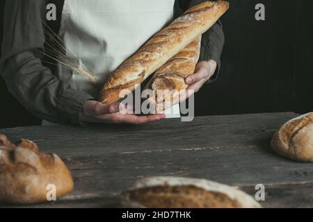 Female hands showing freshly baked french rye loaf on a wooden table. Concept of healthy food and traditional baking. Stock Photo