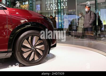 Detail of Nissan Ariya in Tokyo's Ginza Place Nissan Crossing showroom with busy street outside. Selective focus on car. Stock Photo