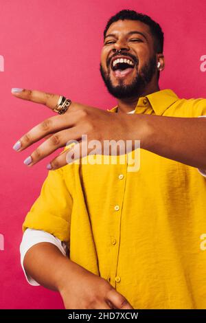 Dancing and streaming in the studio. Happy young man dancing while listening to his favourite music on wireless earphones. Smiling young man standing Stock Photo